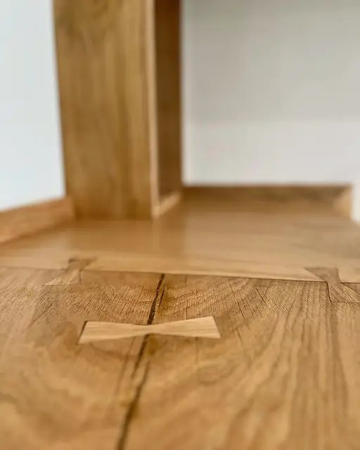Close view of a butterfly key set across the joint between two oak boards, an oak upright softly out of focus behind.