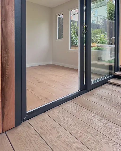 Inside an empty garden room at handover: white walls, a pale wood floor and a black-framed sliding door opening onto a covered composite veranda.