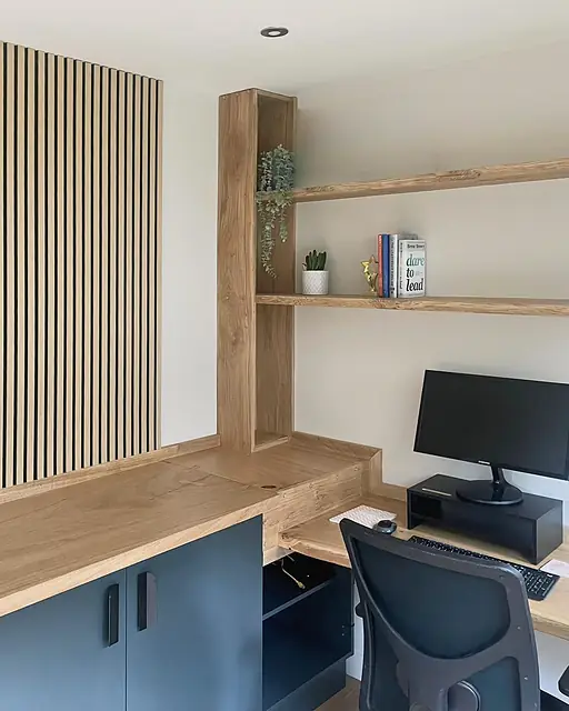 A garden office: an oak slat wall, an L-shaped oak desk over dark cabinets and live-edge oak shelves on an oak upright.