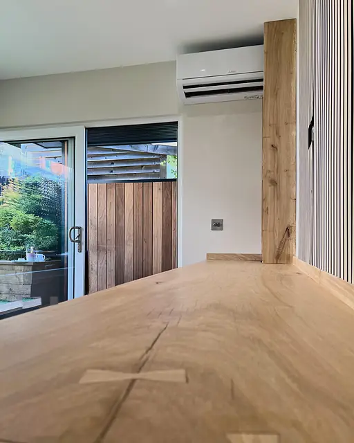 A long oak worktop whose boards are joined with contrasting butterfly keys, beside an oak post and a glazed door to the garden.