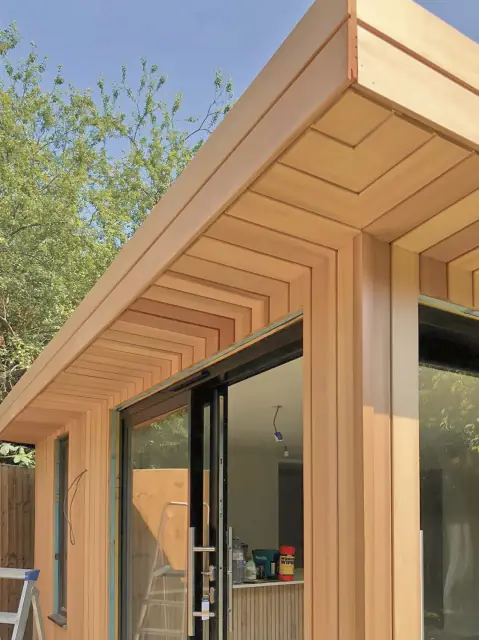A cedar-clad corner with a deep cedar soffit and glass doors, a ladder still leaning inside.