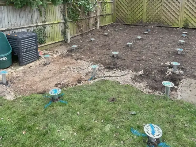 Ground screws set out in rows by the KF Crafts crew across a cleared patch of garden, before any frame goes on.