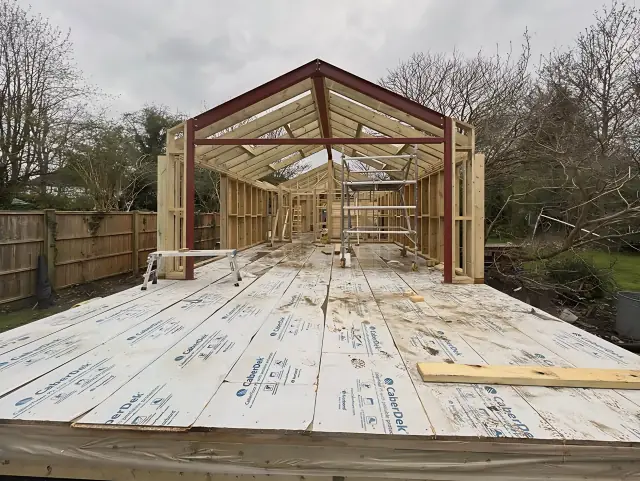 A timber floor deck laid over the base, with the first frames of a gabled building rising above it.