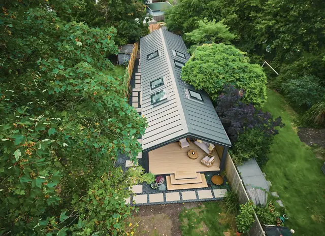 Looking down through trees onto a long gabled garden studio with a grey roof and a small deck.