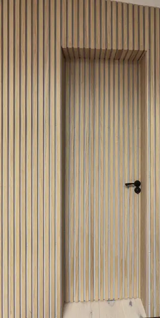A door cut into a wall of vertical timber slats, so that only its black handle gives it away.