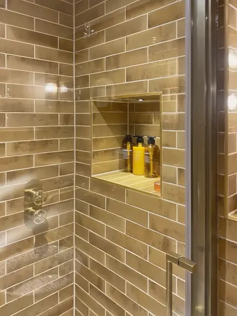 A shower in glazed brick-style tiles with a lit recessed niche and a glass screen.