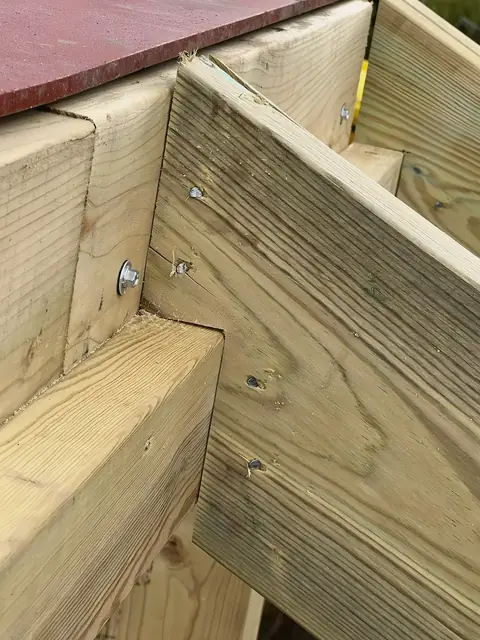 Close up of treated timber joists bolted together beside a red steel beam, the washers and screw heads visible.