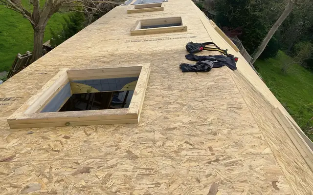Looking along a long roof deck in OSB boards, with timber kerbs framing the rooflight openings, before the roof covering goes on.