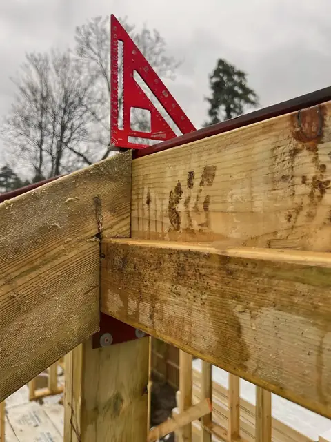 Timber rafters meeting over a red steel beam, with a red rafter square resting on top.