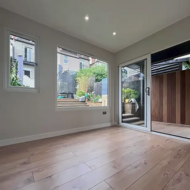 Inside a finished garden room before any furniture: white walls, downlights, a wood-effect floor, two windows and a sliding door onto the porch.
