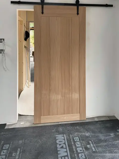 A timber sliding door on a black steel track, being fitted while the floor is still under a protective sheet.